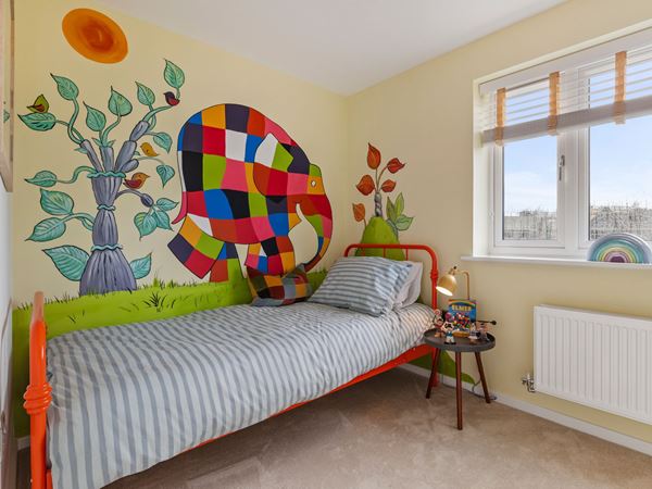 A children's bedroom with an Elmer mural and a red single bed.