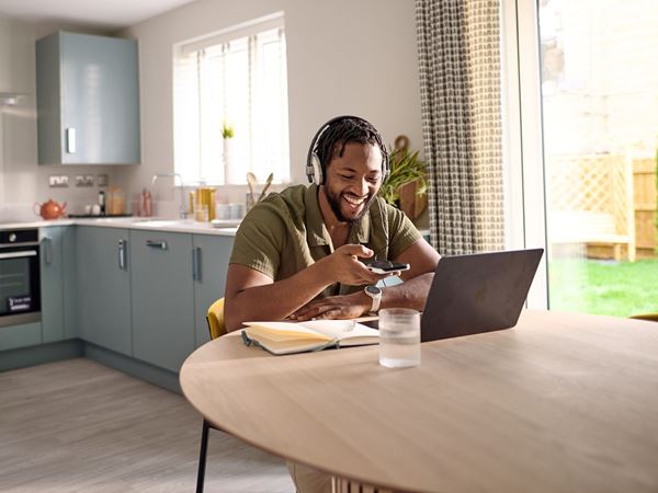 A man sat working at a dinging table in a modern kitchen. 