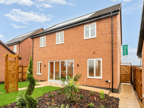 Rear view of a modern brick house with white-framed windows, large sliding glass doors opening to the garden, landscaped flower beds, and a neatly maintained lawn.