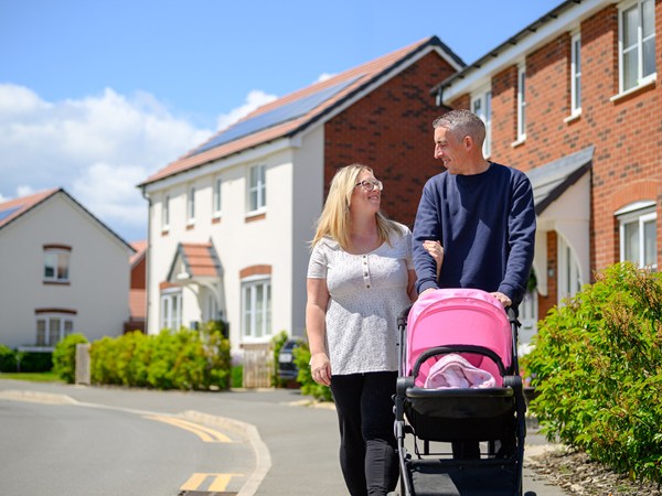 two parents walking wth a pink pram down a street on a Persimmon development