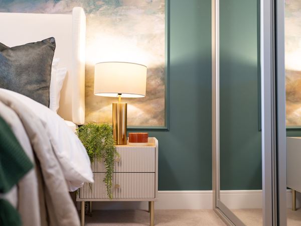 A corner of a modern Persimmon home bedroom with a green feature wall. 