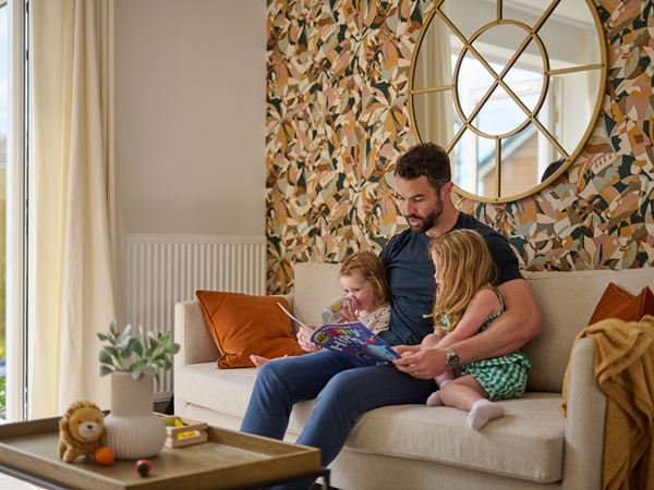 A father sitting on a sofa in a modern new Persimmon home reading to his daughters.