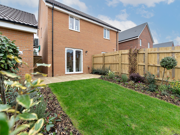 Garden view of brick house with patio and lawn surrounded by planting.