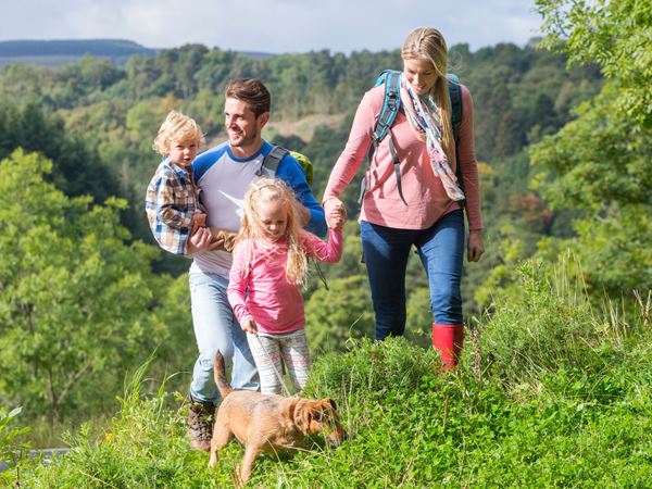 A mother and father walking with their two kids and their dog in the woods. 