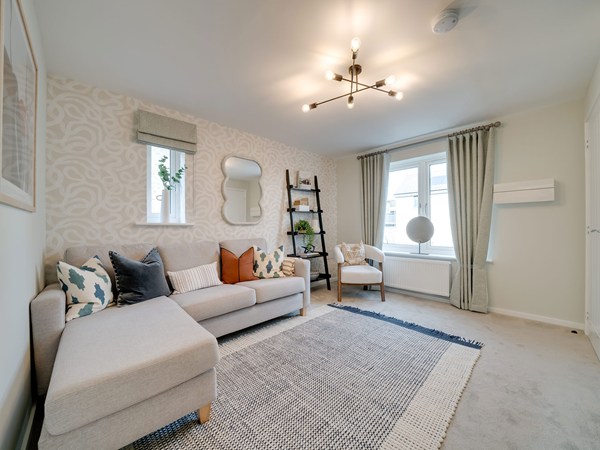 Living room with a corner sofa, feature wall, armchair and large window with neutral curtains.