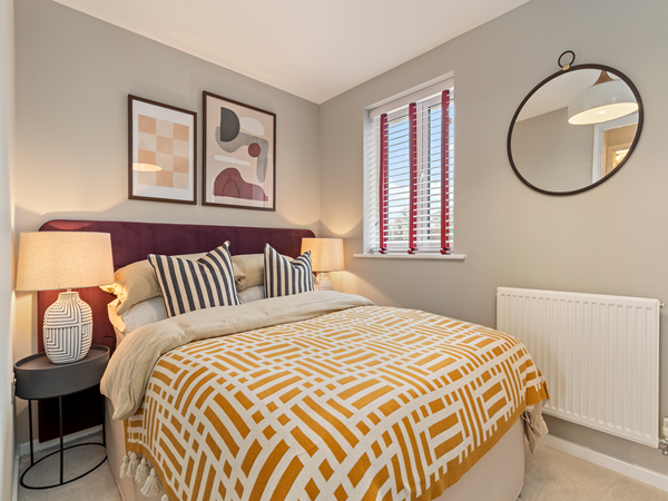 Bedroom with patterned throw, two artworks and window with blinds.