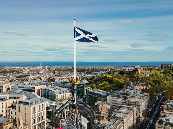 An image of a Edinburgh from above, with a Scottish flag flying on a sunny day with blue skies.