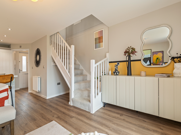 Modern hallway with white staircase, wood flooring and a sideboard with decorative items.