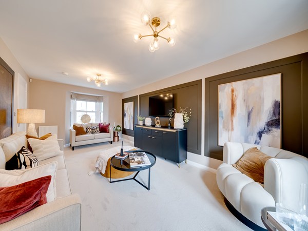 Bright living room with two sofas, a TV mounted on a dark feature wall, abstract artwork, and large glass doors opening to a garden