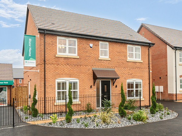 Front exterior of a modern brick detached show home with white-framed windows, a central front door with canopy, landscaped front garden with decorative plants, and a ‘Show Home’ sign displayed.