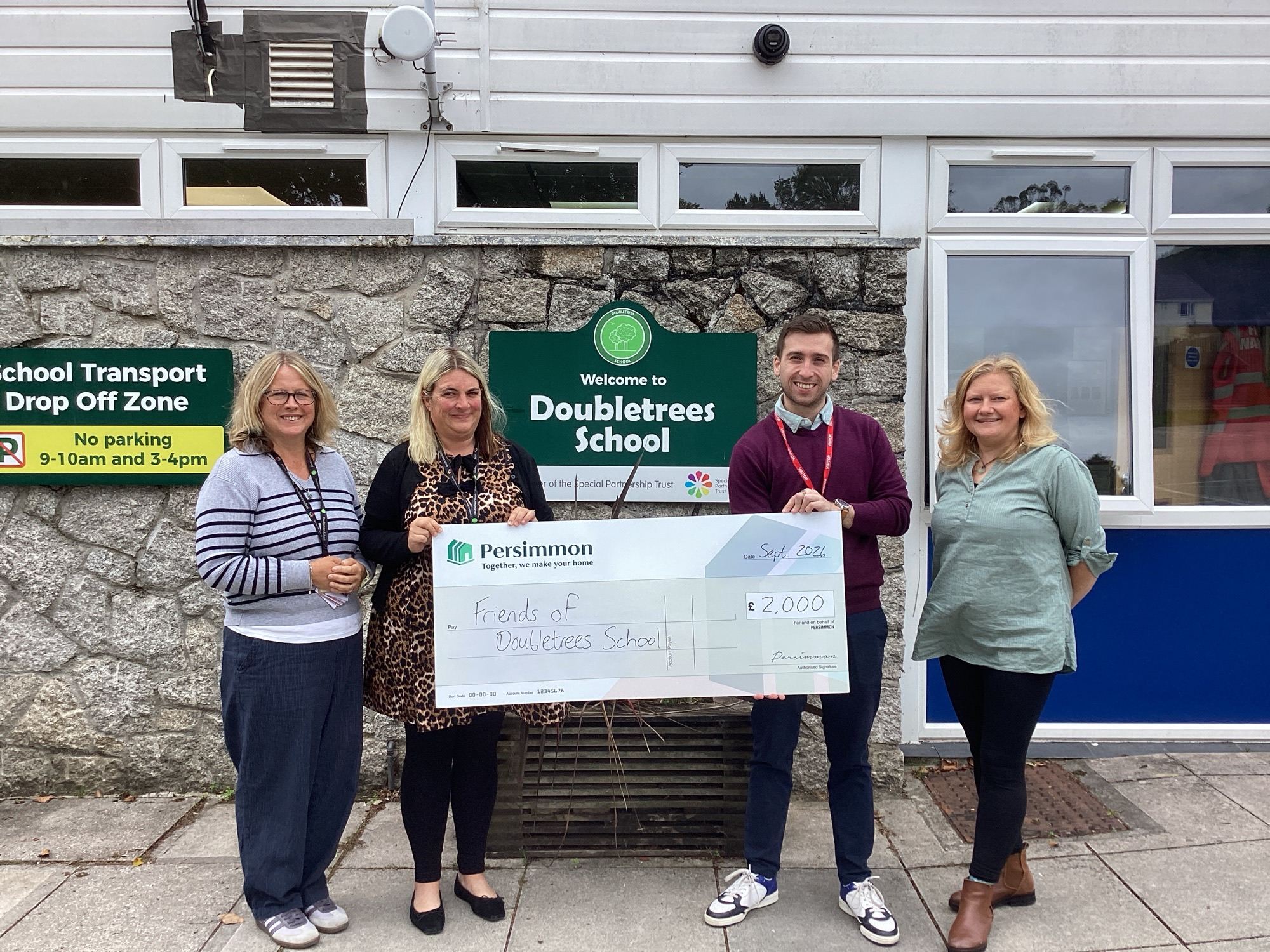 Persimmon Homes representatives present a £2,000 donation cheque to Doubletrees School staff outside the school entrance.