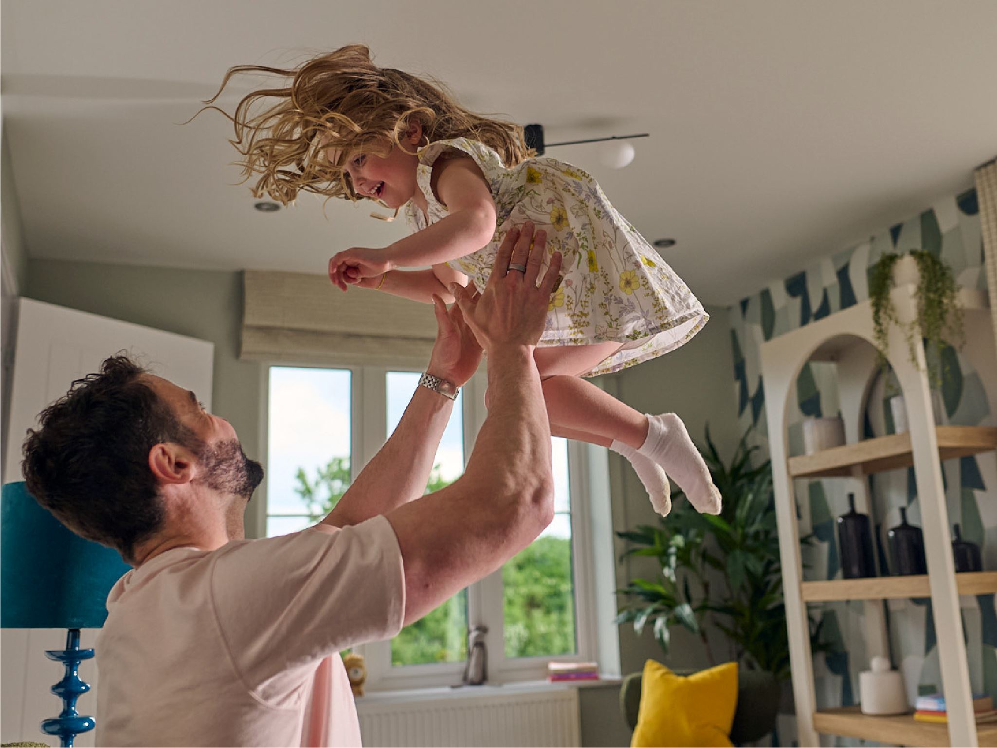 A father throwing his young daughter up into the air in a modern living room. 