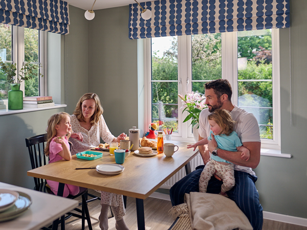 A mother, father and two small daughters sitting at the dining table eating pancakes in a modern Persimmon home.