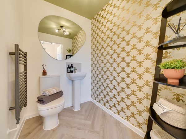 Downstairs WC with toilet and sink. A yellow floral patterned wallpaper to one wall and a large abstract mirror above the sink