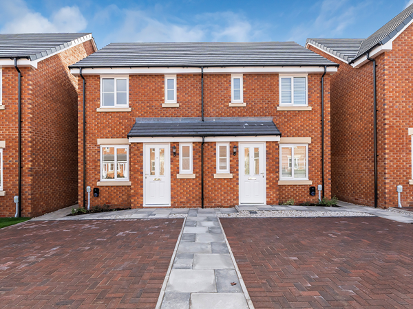 New-build red-brick semi‑detached house with white doors, windows, and paved driveway under a blue sky.