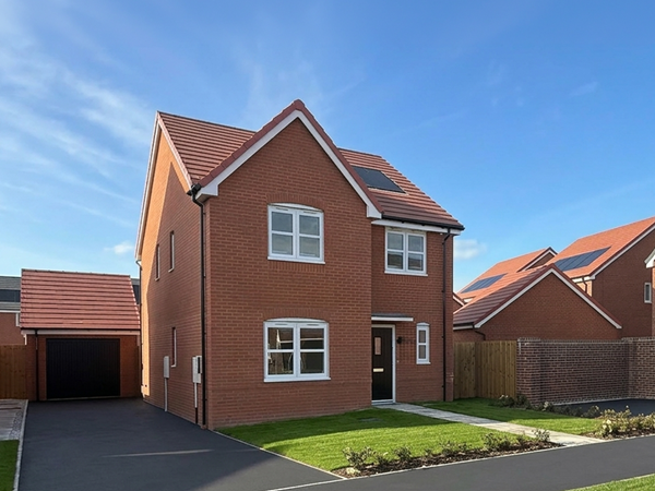 Modern red brick house with a newly paved, black driveway under a bright blue sky with light clouds.