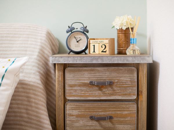 A vintage looking bedside cabinet next to a bed with striped bedding. 