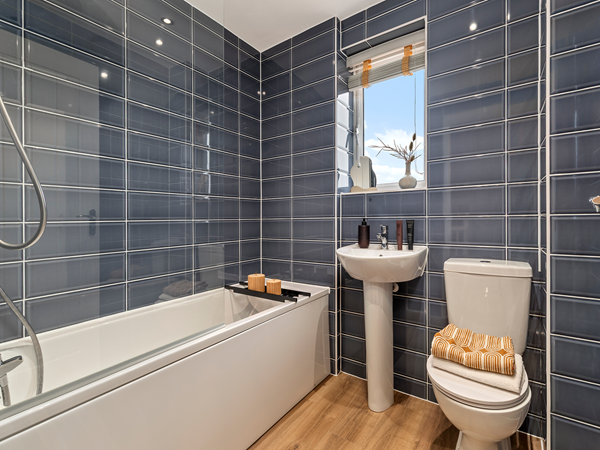 Bathroom with white bathtub, dark tiled walls and pedestal sink.