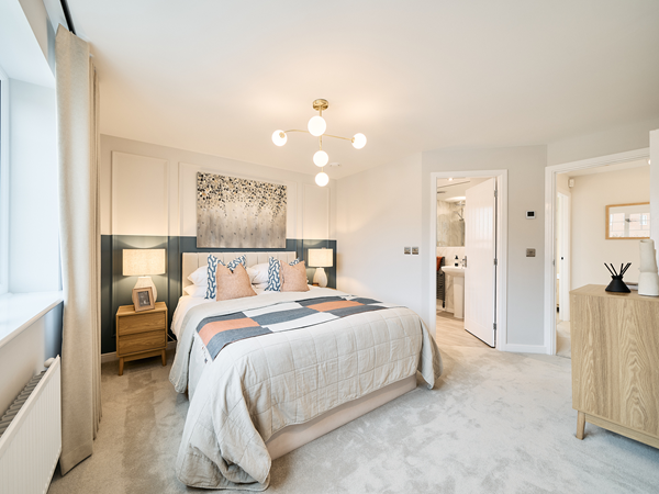 Bright bedroom with modern lighting, upholstered bed, and doorway leading to ensuite bathroom.