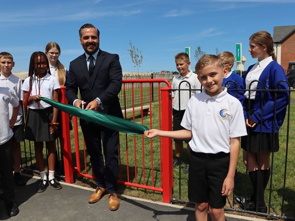 Sales Director cutting the ribbon for a brand new play park at Mulberry Place, Persimmon development, surrounded by school children. 