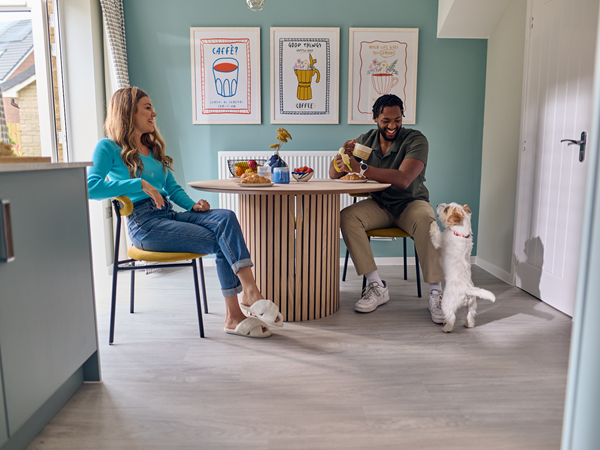 a couple sitting at the breakfast table smiling at their dog