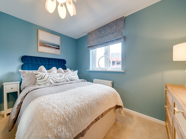 Kielder bedroom with teal walls, double bed and wooden drawers