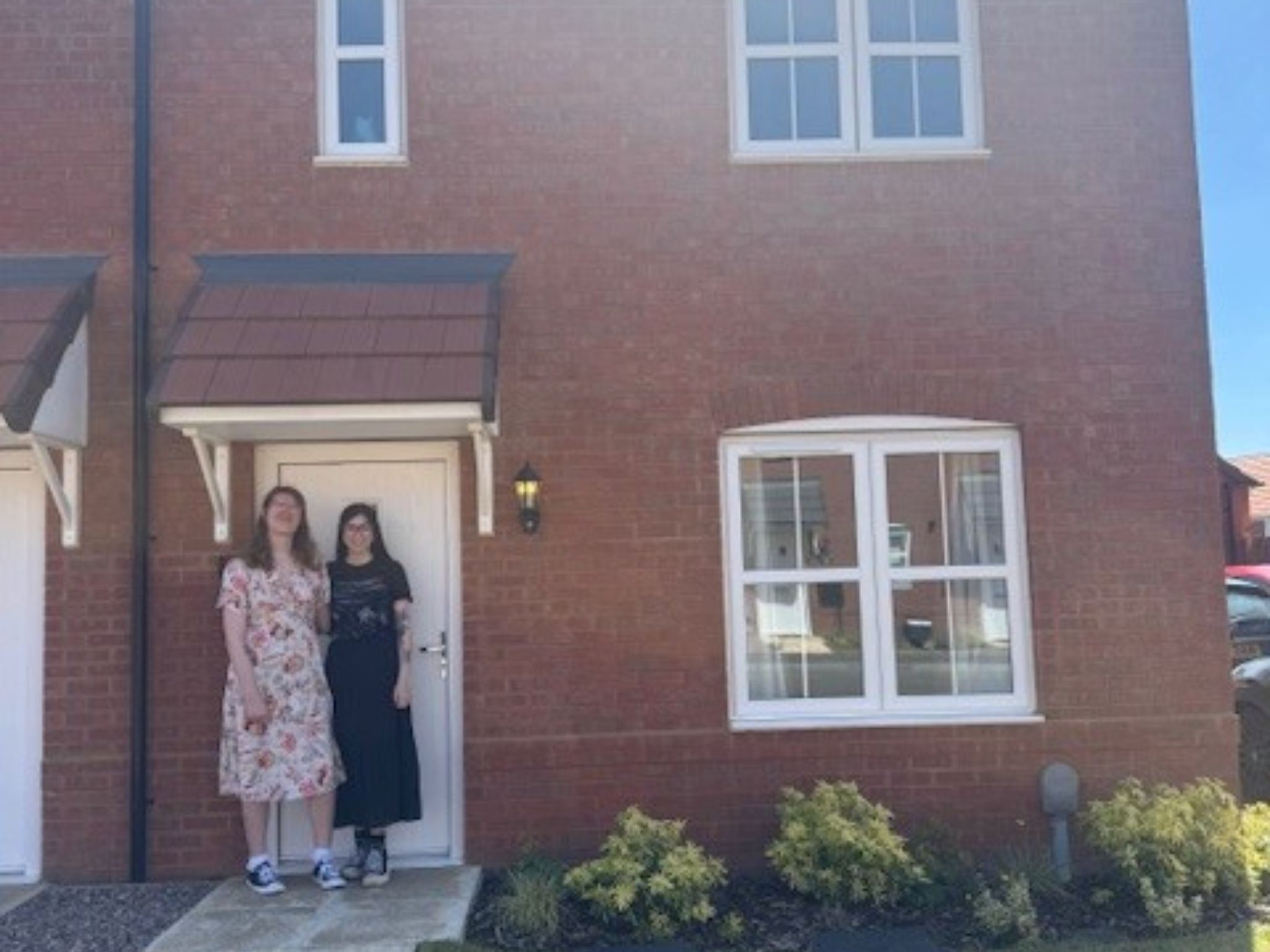 Two female Persimmon home owners stood at the door outside their new home. 