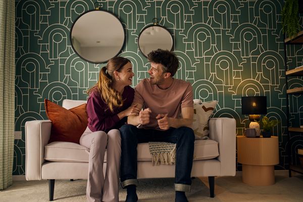 A young couple sitting on the sofa in a new build home by Persimmon, laughing.