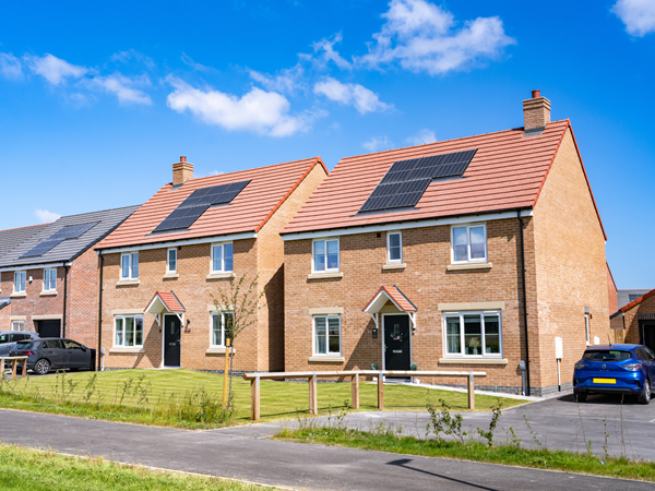 Two red brick double-fronted houses with solar panels and green grass in the foreground.