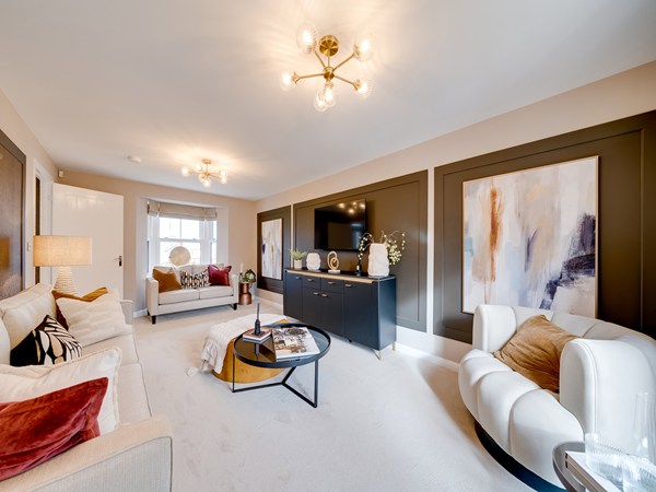 Bright living room with two sofas, a TV mounted on a dark feature wall, abstract artwork, and large glass doors opening to a garden