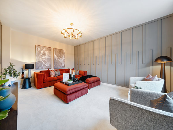 Spacious living room featuring red upholstered sofas and ottomans, soft neutral carpeting, large grey panelled feature wall, modern lighting fixture, and decorative artwork and furnishings.