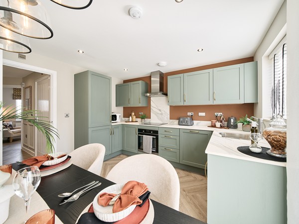 Modern-kitchen-with-sage-green-cabinets-marble-effect-worktops-and-dining-area-with-table-settings.