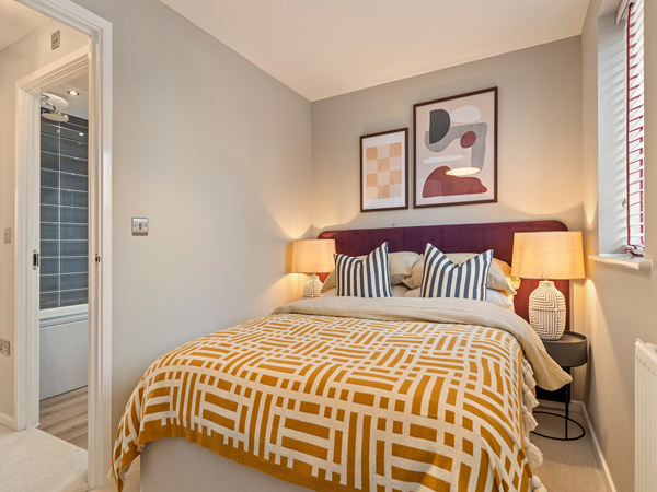 Bedroom with patterned bedding, framed artwork and soft lighting.