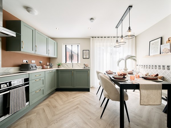 Open-plan-kitchen-and-dining-area-with-sage-green-cabinets-herringbone-flooring-and-pendant-lighting.