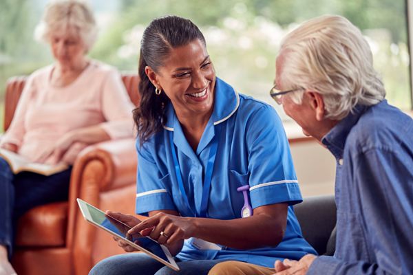 Smiling dark-haired nurse in blue uniform speaking to an elderly man