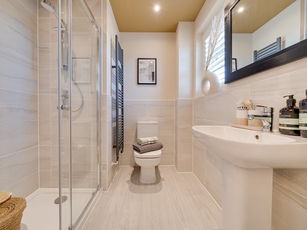 En suite bathroom with shower, sink and toilet. Marble tiles, cream painted walls and mustard colours ceiling