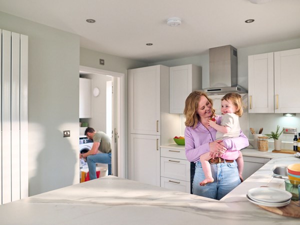 A couple in a bright kitchen with the woman holding a baby and smiling. 