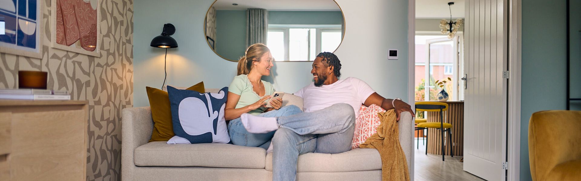 A young couple sat on a sofa in a modern Persimmon living room.